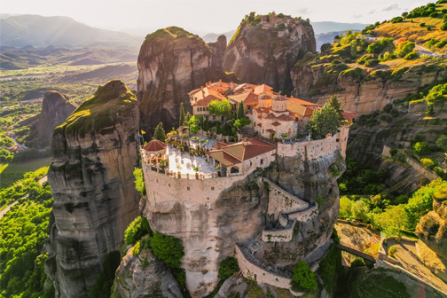 Kloostercomplex Meteora op hoge rotsen met terracotta daken, omringd door groen berglandschap en kronkelende paden.